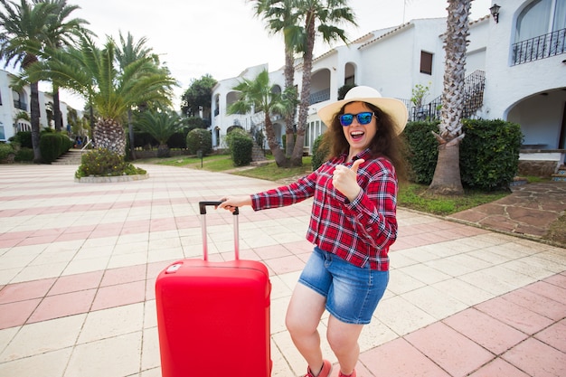 Conceito de viagens, férias, viagens e pessoas - turista mulher com mala aparecendo o polegar