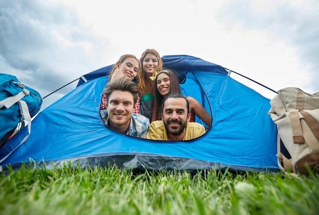 conceito de viagens, turismo, caminhada, equipamentos e pessoas - grupo de amigos felizes com mochilas na barraca no camping