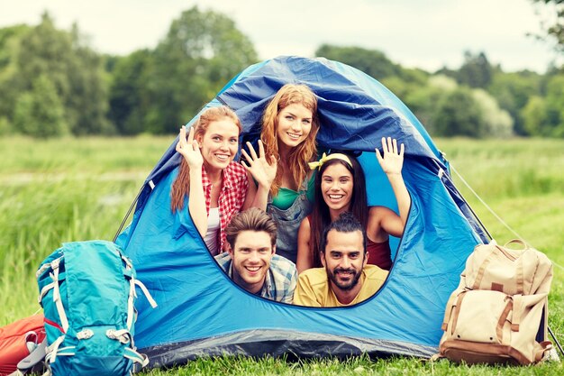 conceito de viagens, turismo, caminhada, equipamentos e pessoas - grupo de amigos felizes com mochilas na barraca no camping