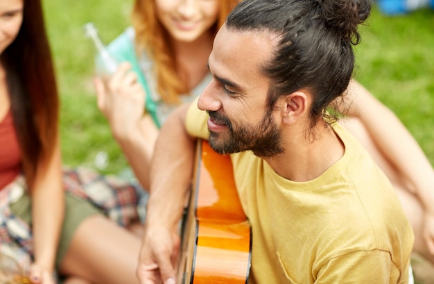 Conceito de viagens, turismo, caminhada, lazer e pessoas - homem feliz com amigos tocando violão no acampamento