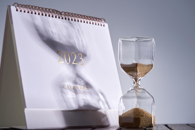 Conceito de vidro de ampulheta e calendário para o tempo escapar ano de boas-vindas 2023