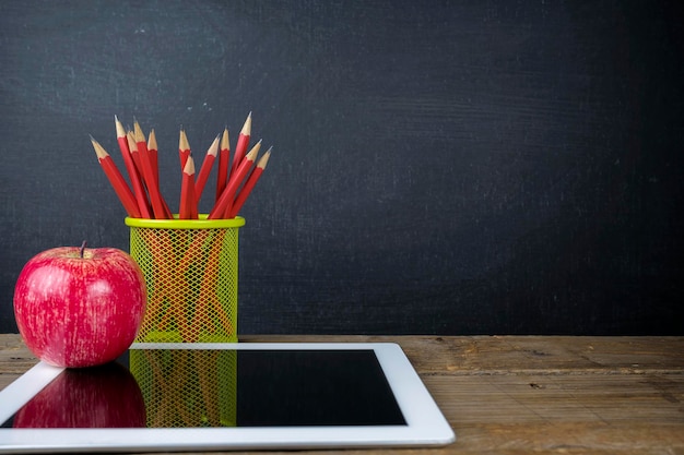 Conceito de volta à escola para obter uma educação aprenda tablet maçã vermelha lápis vermelho na mesa o fundo é um quadro-negro com texto e imagens