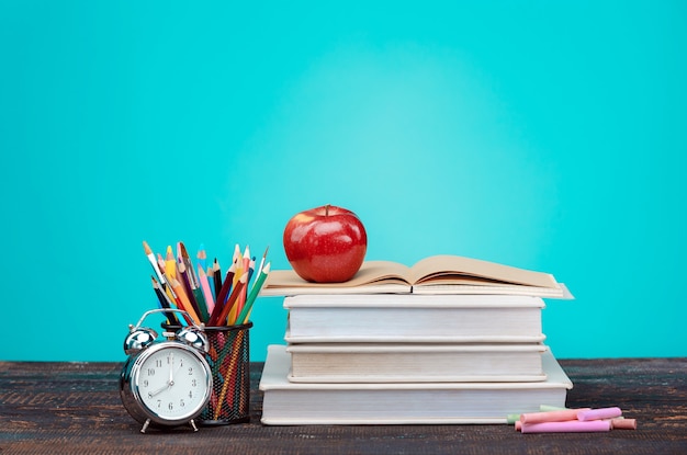 Conceito de volta às aulas. livros escolares, lápis de cor e relógio na parede azul