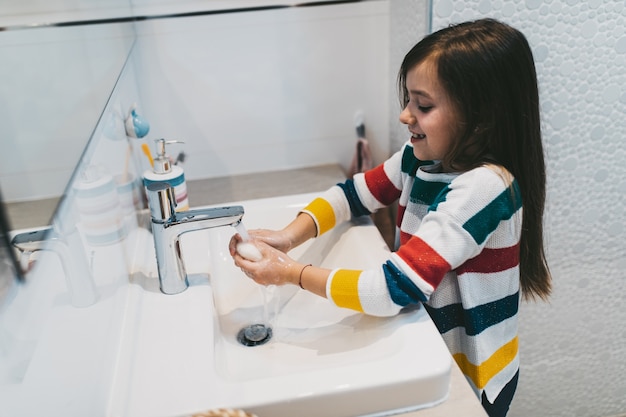 Conceito do Coronavirus COVID-19. Menina lavando as mãos no banheiro com sabonete antibacteriano.