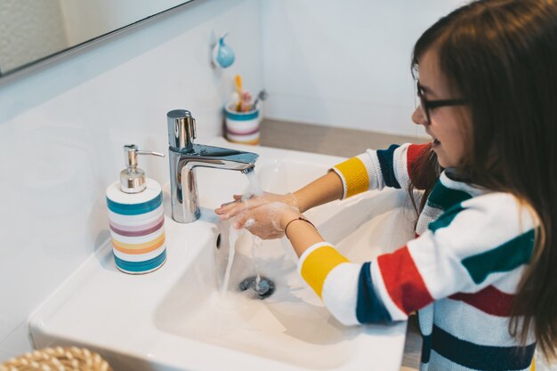Conceito do Coronavirus COVID-19. Menina lavando as mãos no banheiro com sabonete antibacteriano.