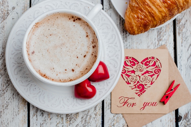 Conceito do dia de Valentim com dois corações, vale-oferta e xícara de café, croissant. Vista do topo