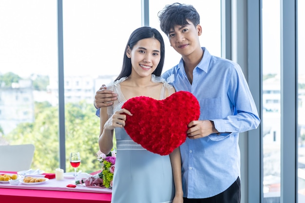 Conceito do dia dos namorados, asiático jovem casal feliz e doce apaixonado segurando um travesseiro em forma de coração vermelho depois do almoço no fundo de um restaurante, casal de história de amor