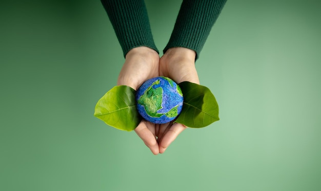 Foto conceito do dia mundial da terra energia verde esg recursos renováveis e sustentáveis cuidados ambientais e ecológicos mãos da pessoa abraçando green leaf and craft globe