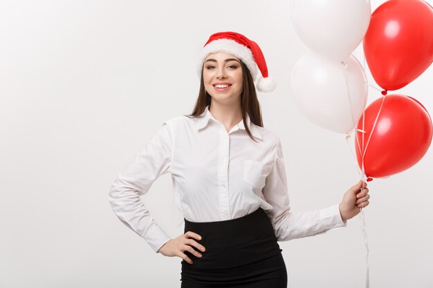 Conceito do negócio - a mulher de negócio segura nova bonita com o chapéu de Santa que guarda o balão comemora para o Natal.