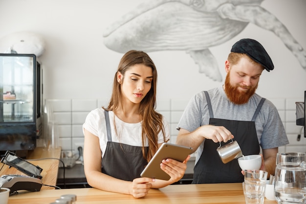 Conceito do negócio do café - baristas alegres que olham seus comprimidos para pedidos on-line no café moderno.