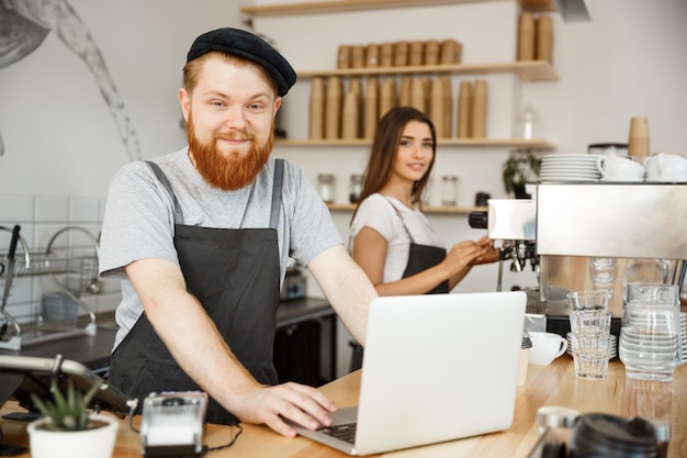 Foto conceito do negócio do café - bartende, barista ou gerente barbeiro bonito bonito e trabalhando e planejando no laptop no café moderno.