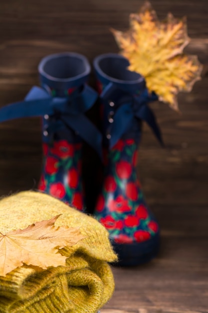 Conceito do outono: roupa morna da criança e botas de borracha no fundo de madeira marrom.