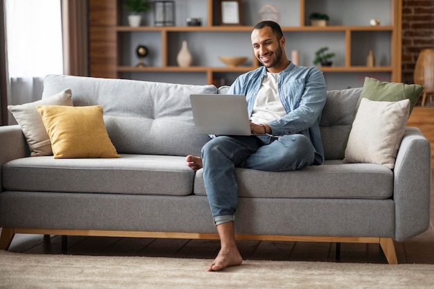 Conceito freelance feliz jovem afro-americano usando laptop em casa