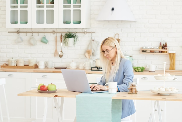 Conceito freelance. Mulher de negócios bonita em roupas casuais e óculos está examinando documentos e sorrindo enquanto trabalhava com um laptop na cozinha