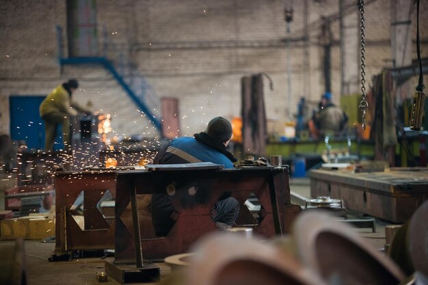 Conceito industrial. Um homem sentado em seu local de trabalho e usando o moedor. O fogo brilha. Vista traseira