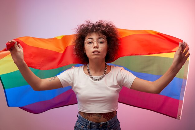 Foto conceito lgbtq. menina caucasiana positiva com cabelo afro encaracolado segurando a bandeira do arco-íris isolada