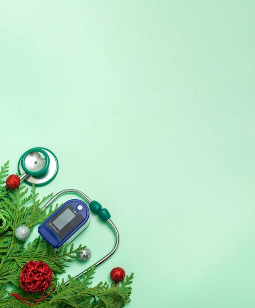 Conceito médico: celebrar o Natal na área da saúde. Vista superior de um close-up plano leigo de um estetoscópio, oxímetro de pulso com ramos de abeto, sobre um fundo verde. Com espaço de cópia. Foto vertical