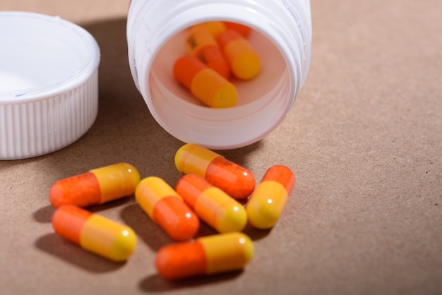 Conceito médico e de saúde: garrafa de medicamentos aberta, montes de cápsulas espalhadas em fundo marrom.