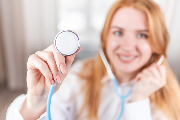 Conceito médico Enfermeira sorridente com aparelho e um estetoscópio na mão Médica feliz e rindo em um jaleco branco posando para a câmera Funcionário do hospital