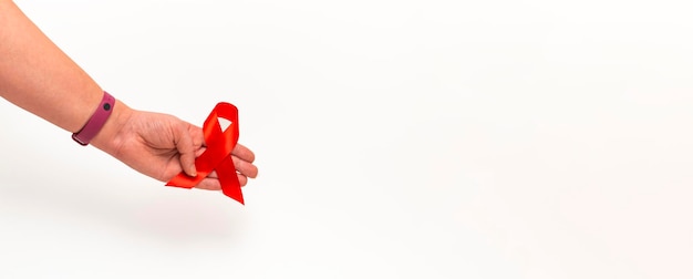 Conceito médico para o dia mundial da aids em dezembro. a fita vermelha de conscientização sobre a aids agarrada pela mão de uma mulher em um fundo branco. fechar-se