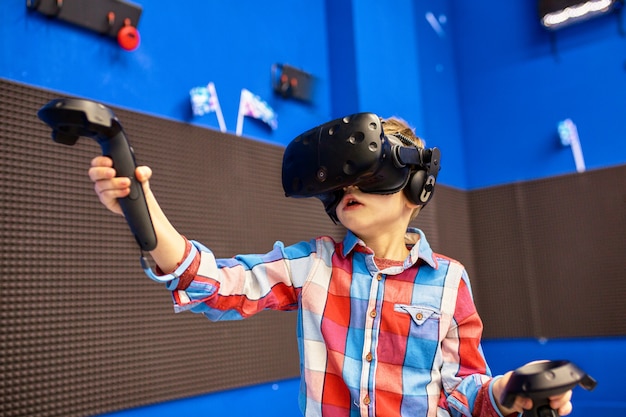 Conceito moderno de tecnologia, jogos e pessoas - menino no fone de ouvido da realidade virtual ou óculos 3d jogando videogame no game center