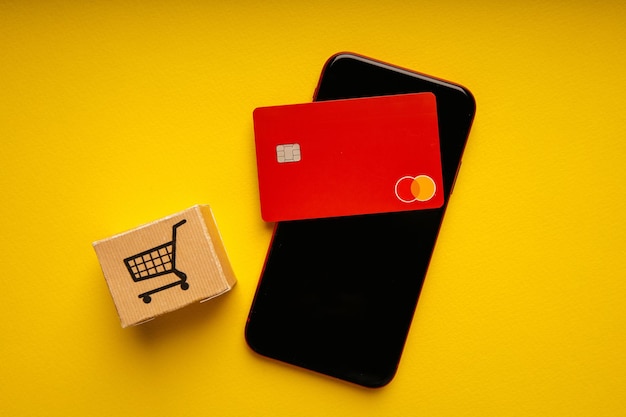 Conceito online de compras e pagamento de cartões de crédito Caixa de entrega com carrinho e smartphone