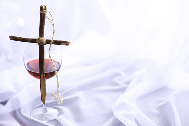 Conceito religioso. Cruz de madeira feita à mão em um fundo branco. Candeeiro de vidro de vinho com velas.