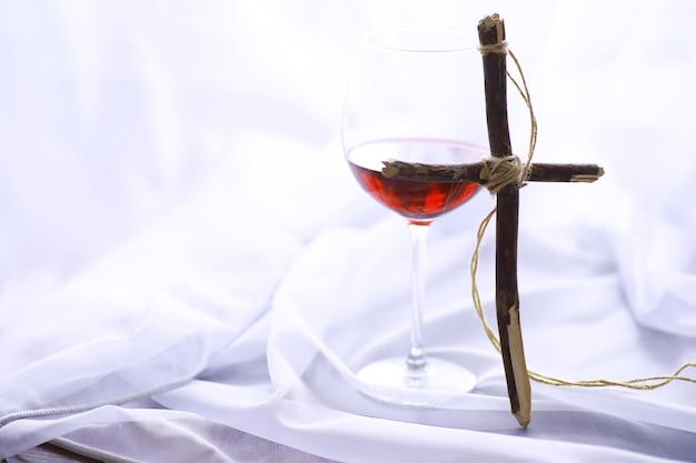 Conceito religioso. Cruz de madeira feita à mão em um fundo branco. Candeeiro de vidro de vinho com velas.