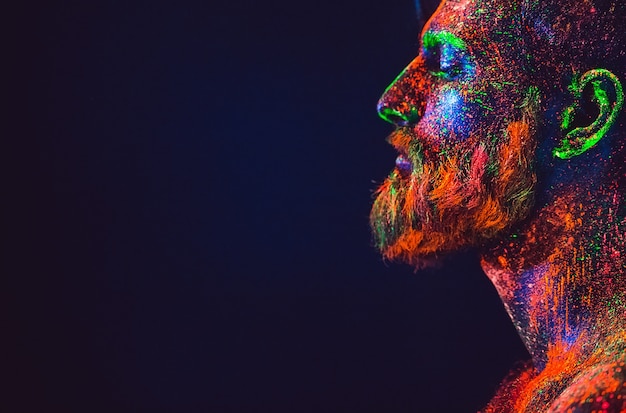 Conceito. Retrato de um homem barbudo. O homem é pintado em pó ultravioleta.