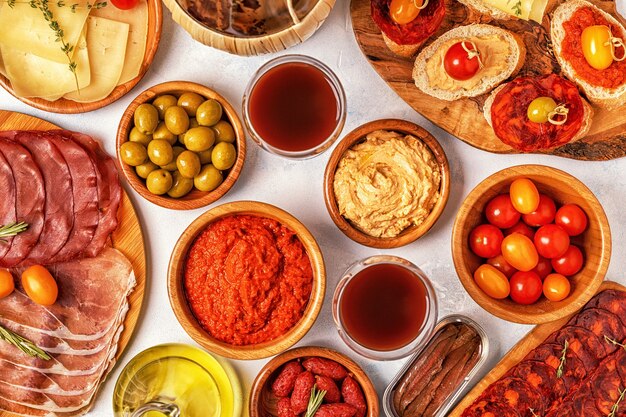 Conceito típico de tapas espanholas. O conceito inclui fatias de jamon, chouriço, linguiça, tigelas com azeitonas, tomates, anchovas, purê de grão de bico, queijo.