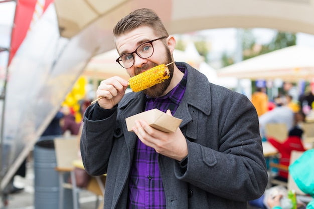 Conceito vegetariano e de refeição - homem bonito comendo milho de comida de rua no festival de fast food