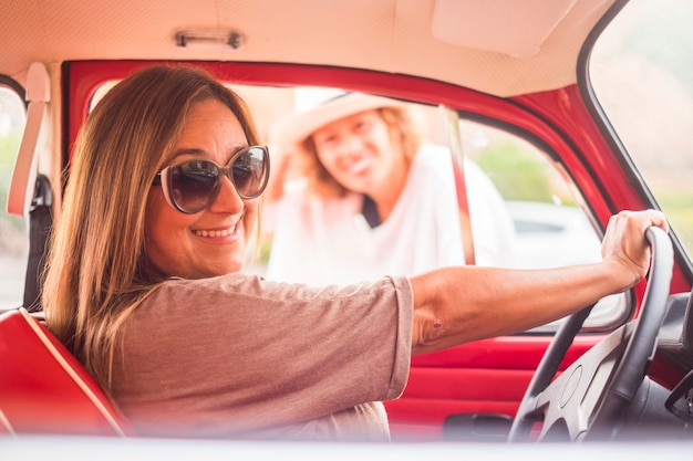 conceito vintage e retro com duas mulheres na amizade juntamente com um carro vermelho lendário. liberdade e conceito de estilo de vida alternativo