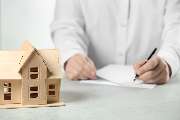 Conceitos de construção e lei fundiária homem escrevendo na mesa branca com foco no modelo da casa