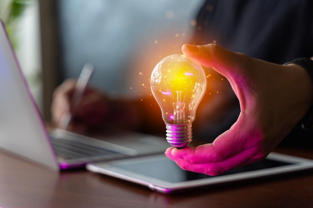 Conceitos de contabilidade e criatividade Empresário segurando lâmpada brilhante na mesa de madeira com computador portátil como solução de negócios e criativa