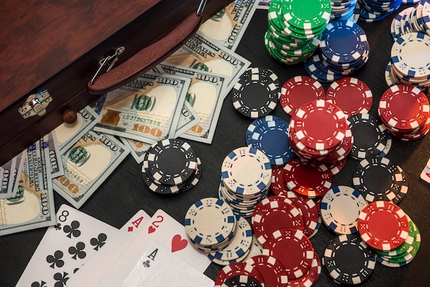 Conceitos de jogos de azar. Apostar é uma aposta para os investidores. Caixa cheia de fichas, dólares e cartas de jogar em uma parede preta