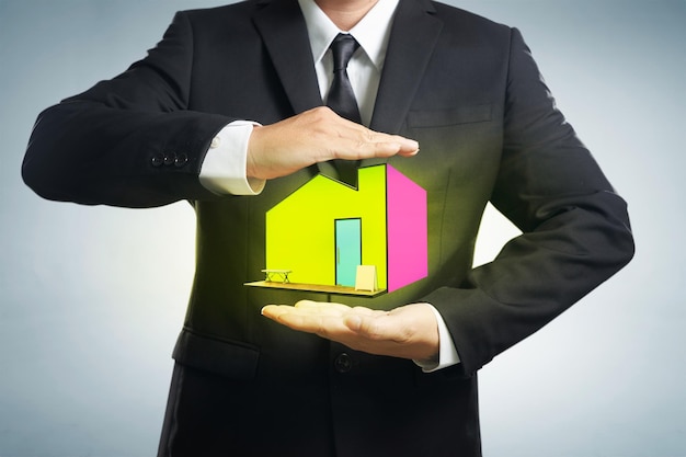 Conceitos de seguro residencial Empresário com gesto protetor e ícone de casa com fundo cinza