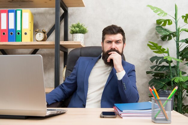 Concentração e foco Chefe barbudo sentado no escritório com laptop Gerente resolvendo problemas de negócios Empresário encarregado de soluções de negócios Desenvolvendo estratégia de negócios Negócios arriscados