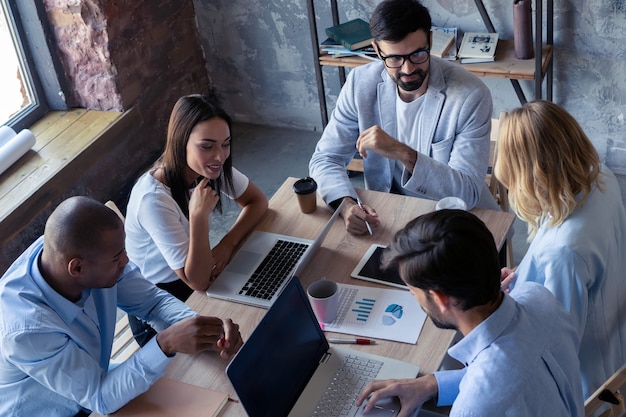 Concentração total no trabalho. Grupo de jovens empresários trabalhando e se comunicando enquanto estão sentados na mesa do escritório com colegas sentados ao fundo.