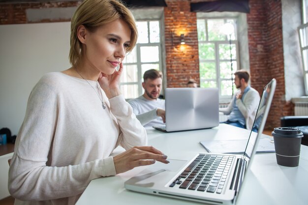 Concentrada jovem empresária linda trabalhando no laptop no escritório moderno brilhante.