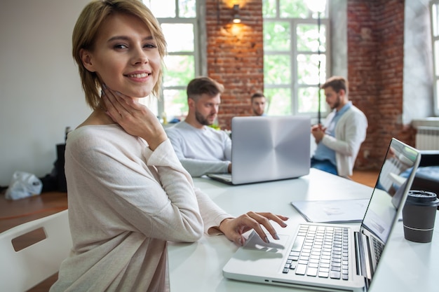 Concentrada jovem empresária linda trabalhando no laptop no escritório moderno brilhante.