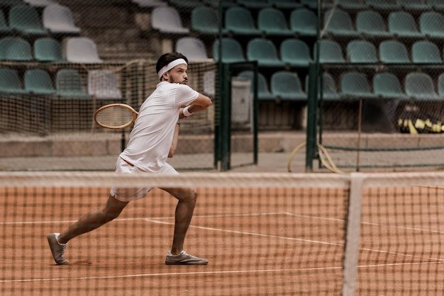 Concentrado apuesto hombre de estilo retro jugando al tenis en la cancha