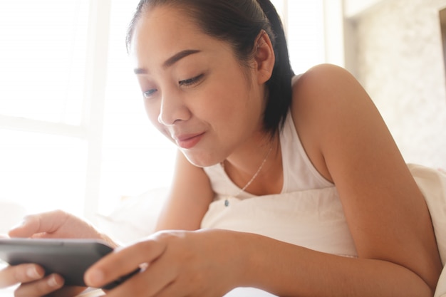 Concentrado de mulher expressão rosto de mulher joga jogo móvel on-line em sua cama no quarto.