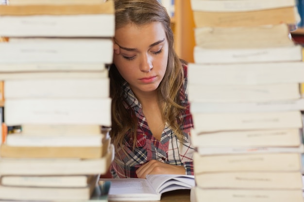 Concentrado estudiante bonita estudiando entre pilas de libros