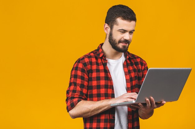 Concentrado en el trabajo. Hombre hermoso joven confidente en el trabajo casual en la computadora portátil mientras que se coloca.