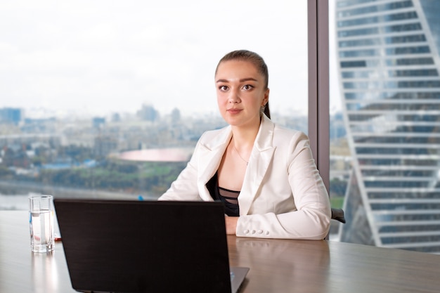 Concentrado en el trabajo. Mujer joven segura en ropa casual elegante trabajando en la computadora portátil mientras está sentado cerca de la ventana en la oficina creativa