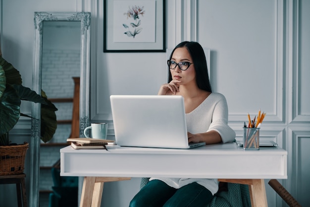 Concentrando-se no projeto. mulher jovem e bonita trabalhando no computador enquanto está sentada no escritório em casa