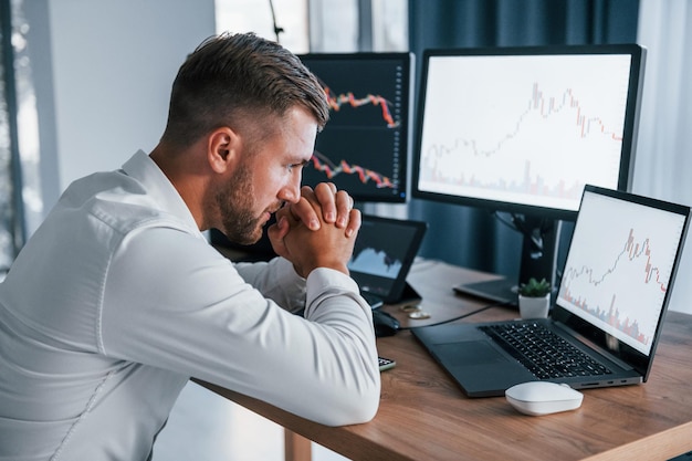 Concentrando-se no trabalho Jovem empresário em roupas formais está no escritório com várias telas