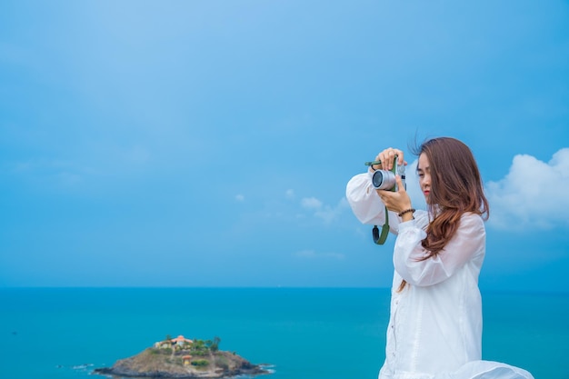 Concentre-se jovem feliz vestindo vestido branco segurando uma câmera para tirar fotos para manter memórias