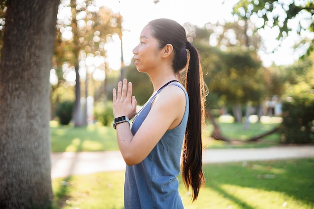 Concentre-se menina asiática fazendo exercícios de ioga ao ar livre no parque com raios de sol ao fundo