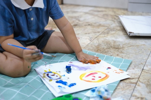 Foto concentre-se nas mãos no papel, na aprendizagem da primeira infância usando tintas e pincéis para desenvolver a imaginação e aprimorar as habilidades no quadro.